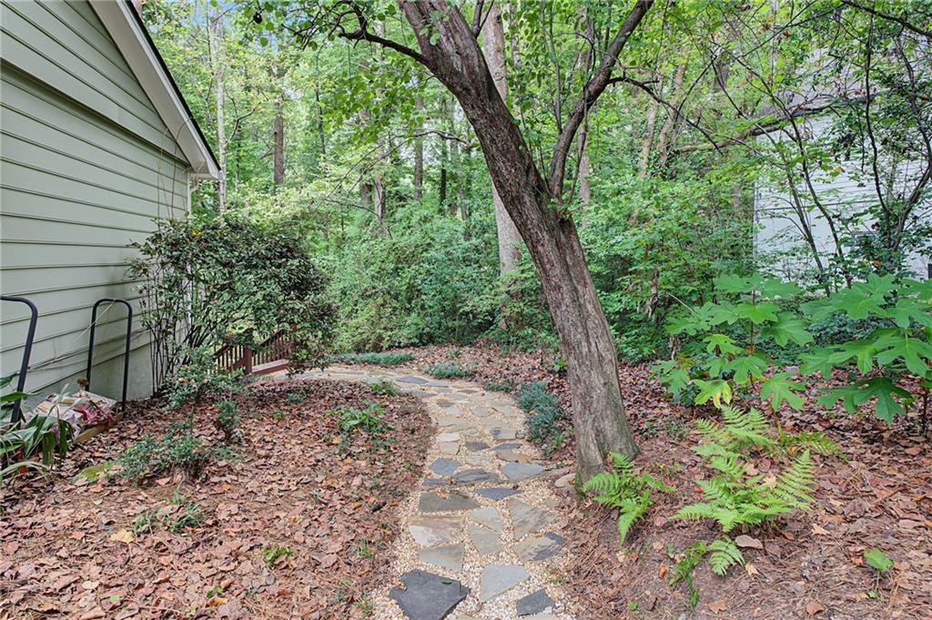 Stone path winding through a wooded backyard beside the home, beneath a large mature tree.
