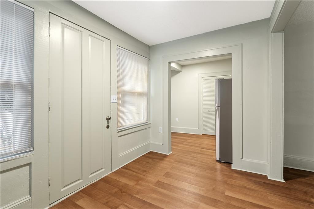 Interior entry area with paneled front door, shaded windows, wood flooring, and a refrigerator beyond.