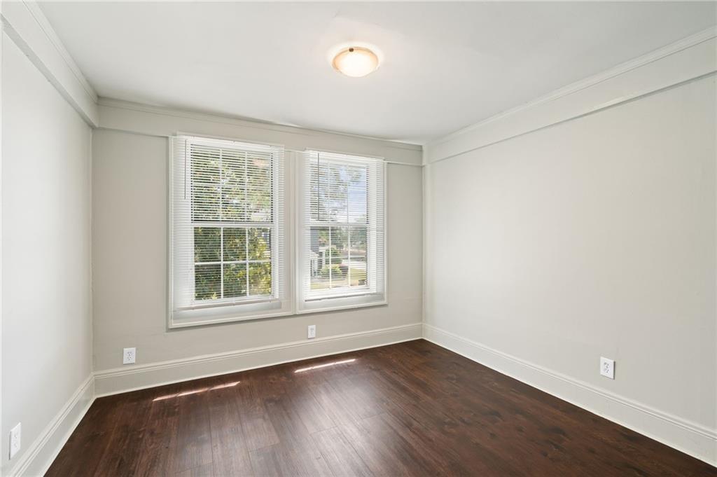 Empty room with dark wood flooring and two windows with white blinds.