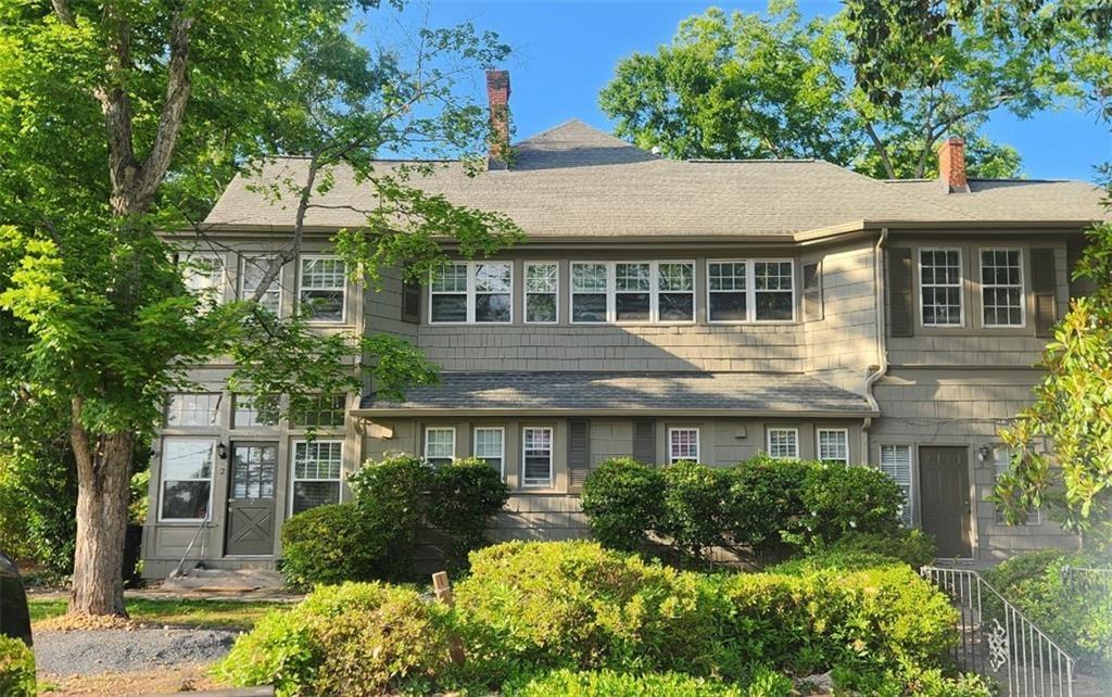 Gray two-story home with a long row of upper windows, framed by mature trees and shrubs.