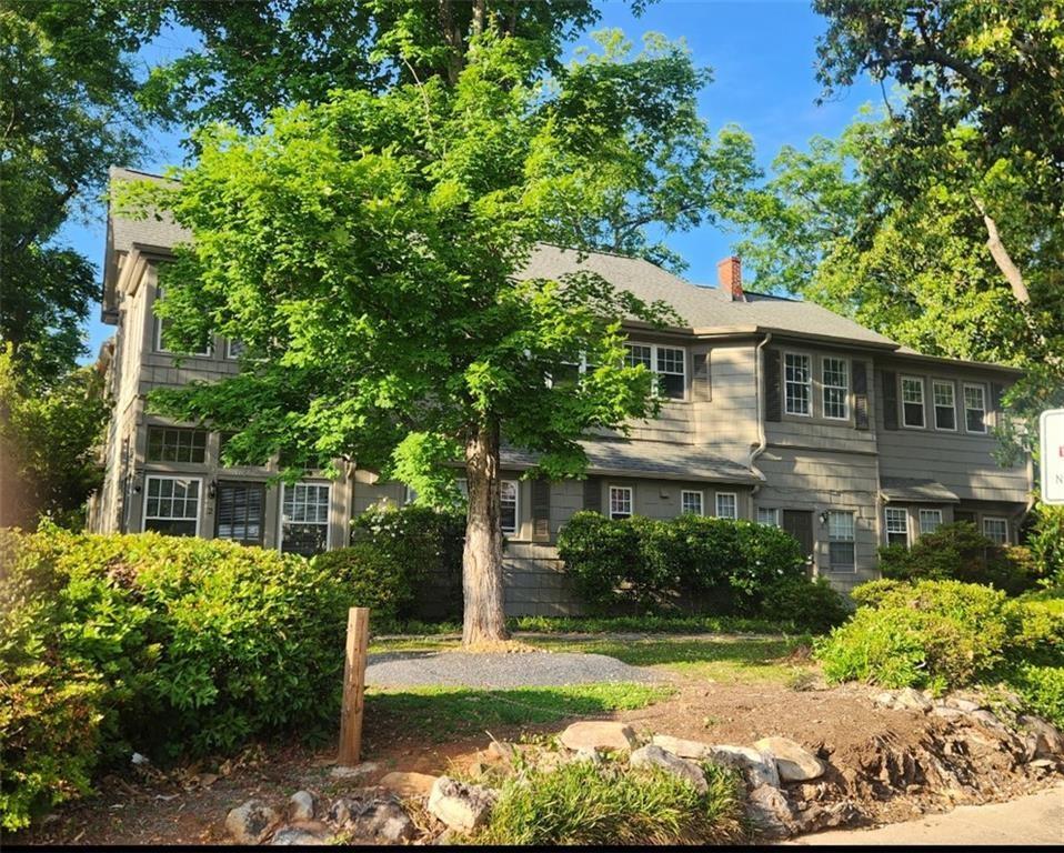 Gray multi-story building partly screened by a large tree and landscaped shrubs.