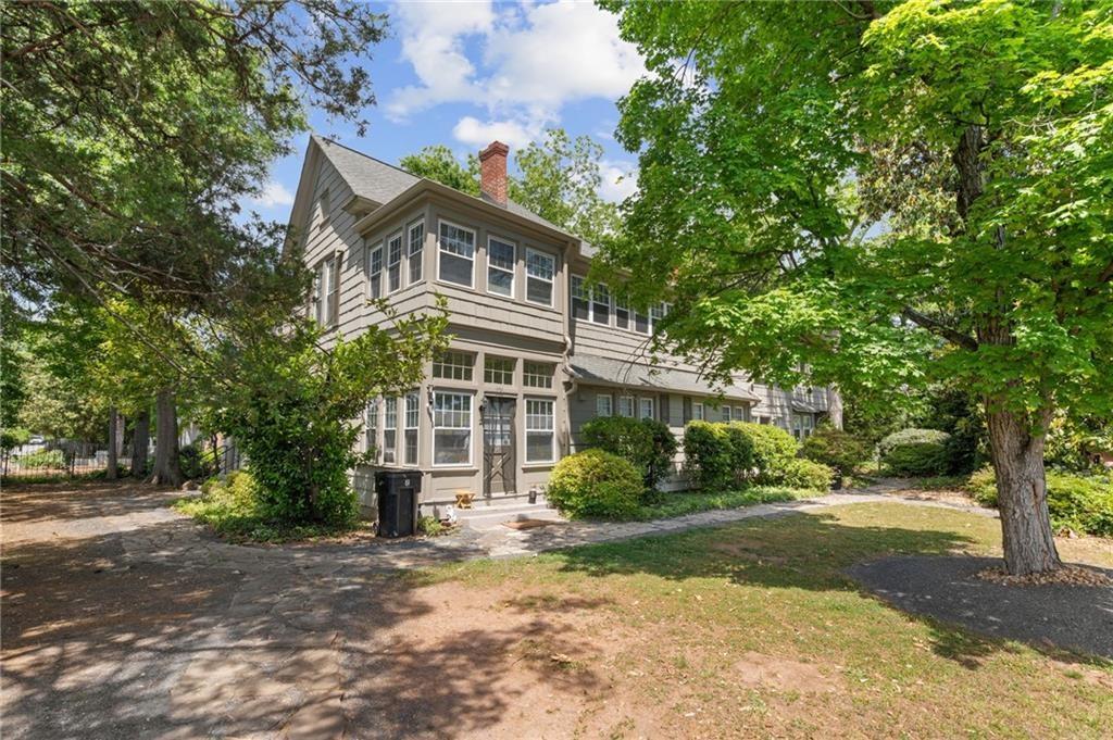Two-story gray house with a gabled roof, large windows, and mature trees in the front yard.