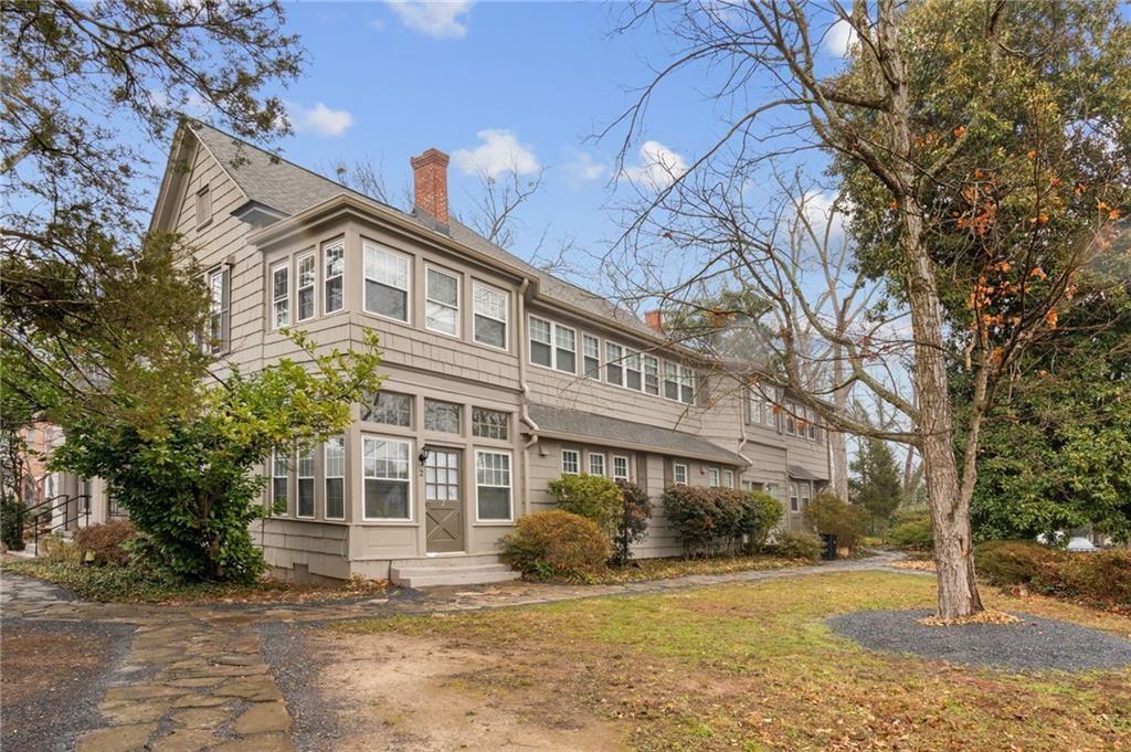 Two-story gray-sided house with a long row of windows, entry steps, and mature trees.