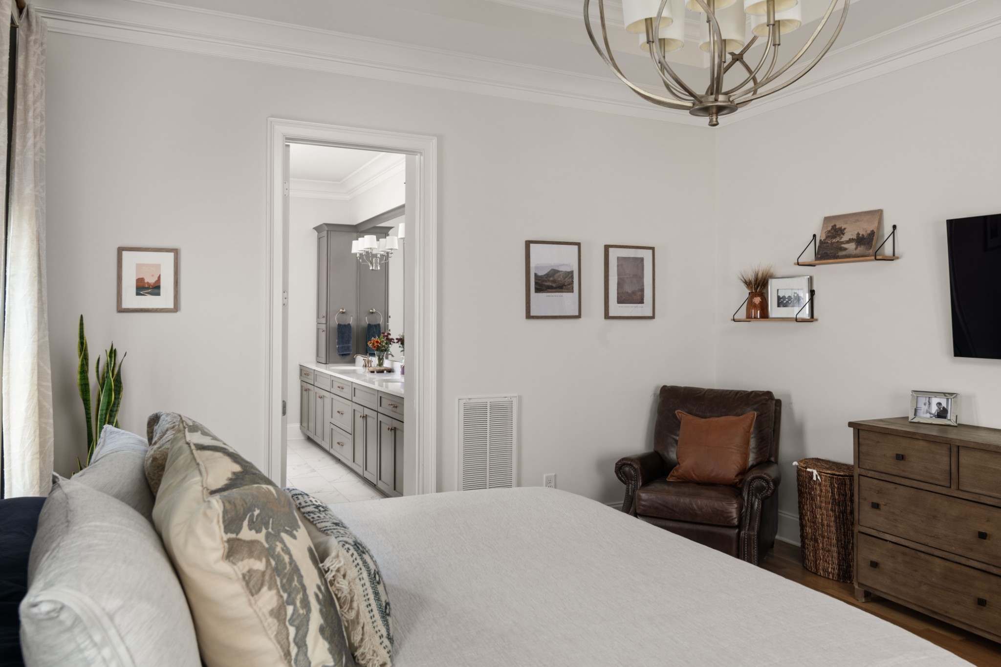 Bedroom with a large bed, leather armchair, and doorway to a vanity area.