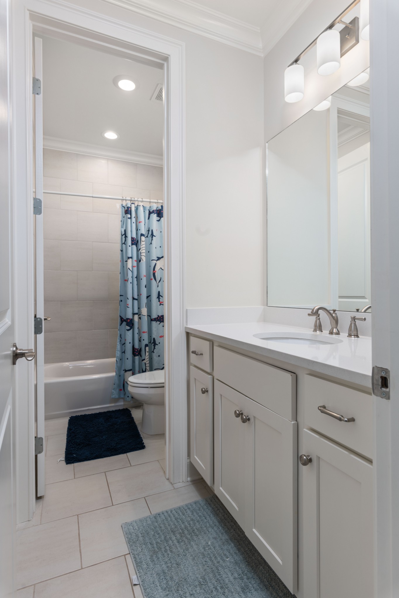 Bathroom with a white vanity and mirror, tiled tub-shower, and blue patterned curtain.