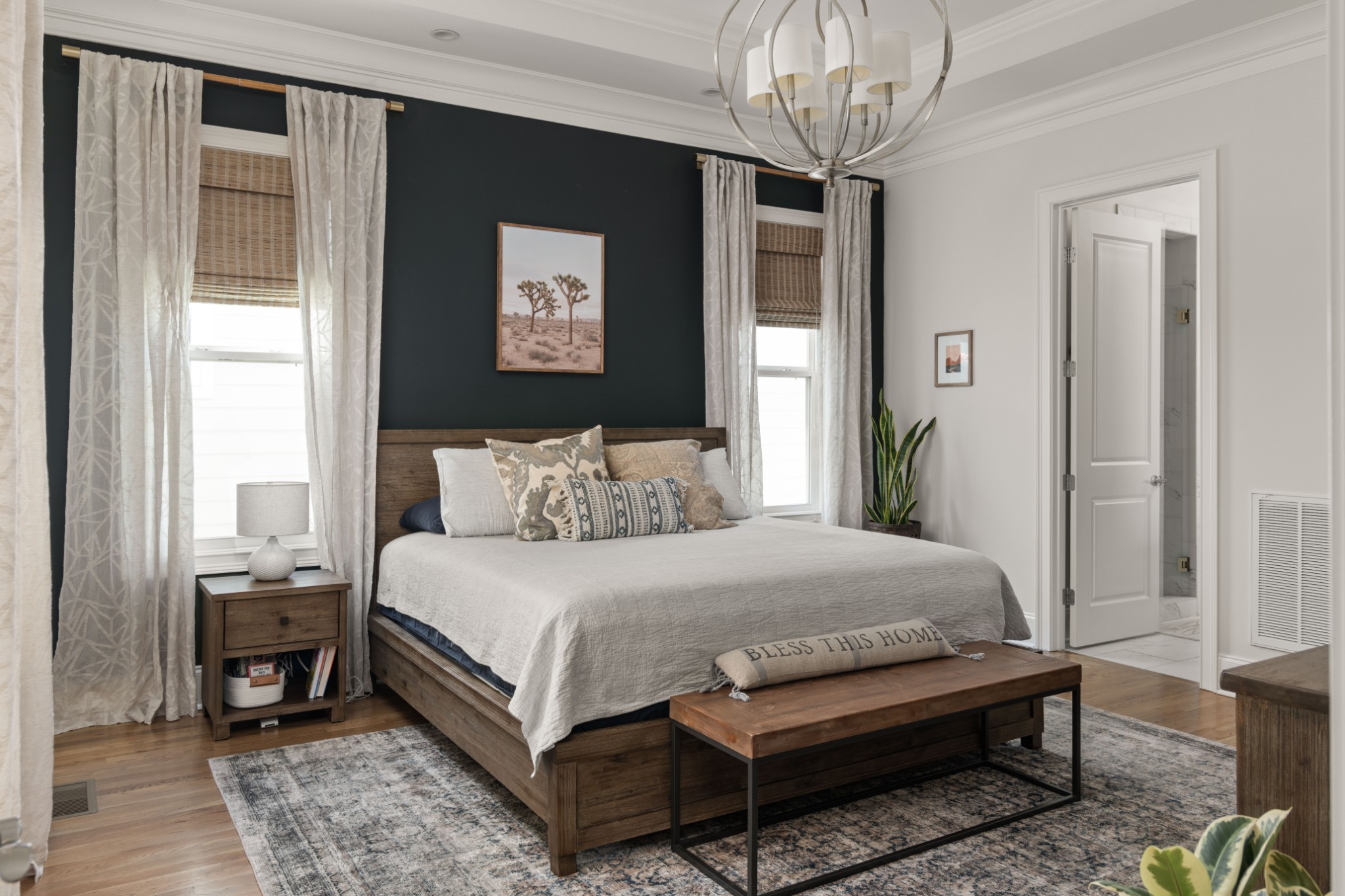 Bedroom with a dark accent wall, wood bed, layered neutral bedding, and an adjoining bathroom doorway.
