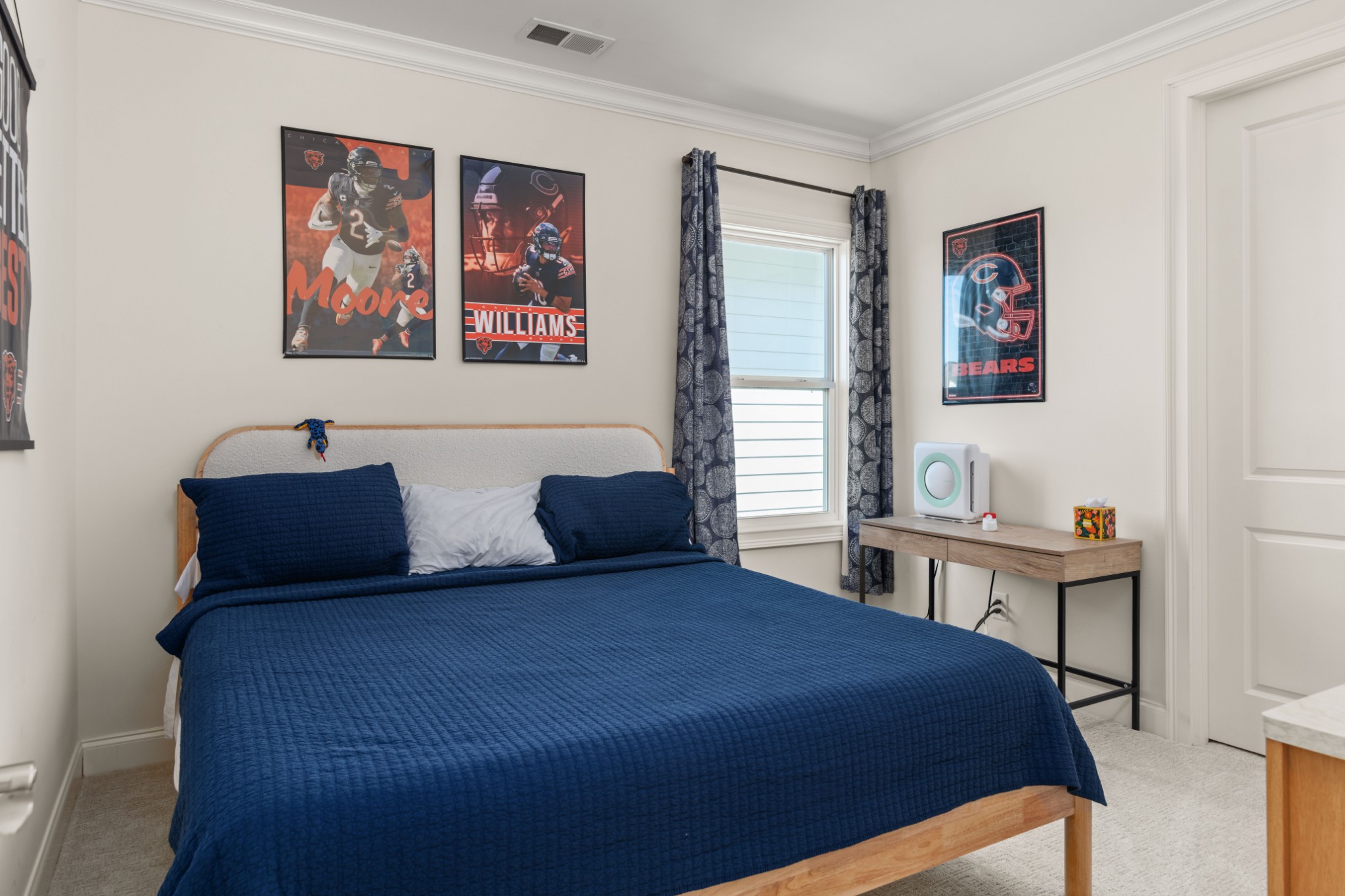 Bedroom with a navy quilted bed, Chicago Bears posters, and patterned curtains.