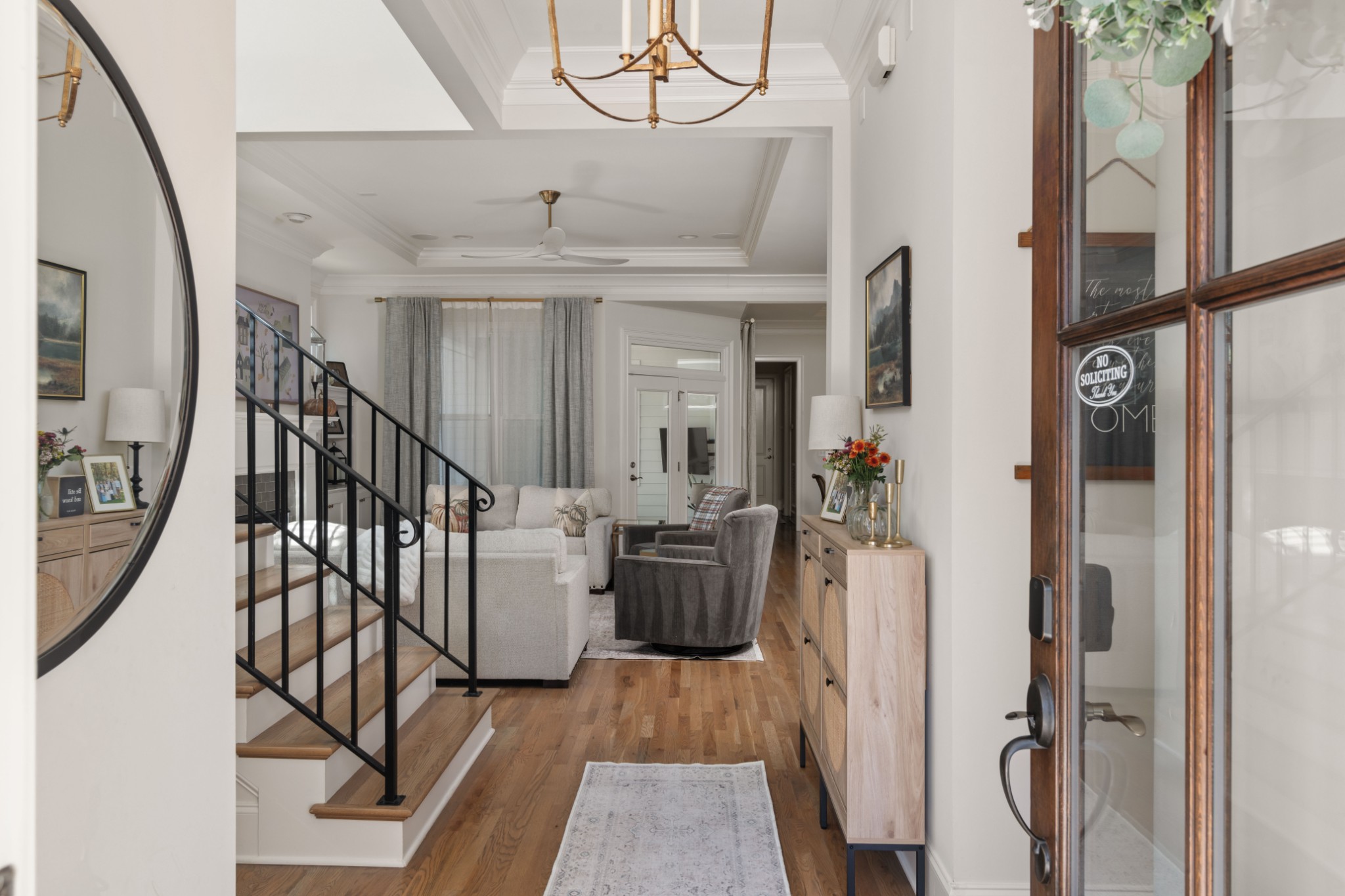 Entryway opening to a furnished living room, with a black-railed staircase and hardwood floors.