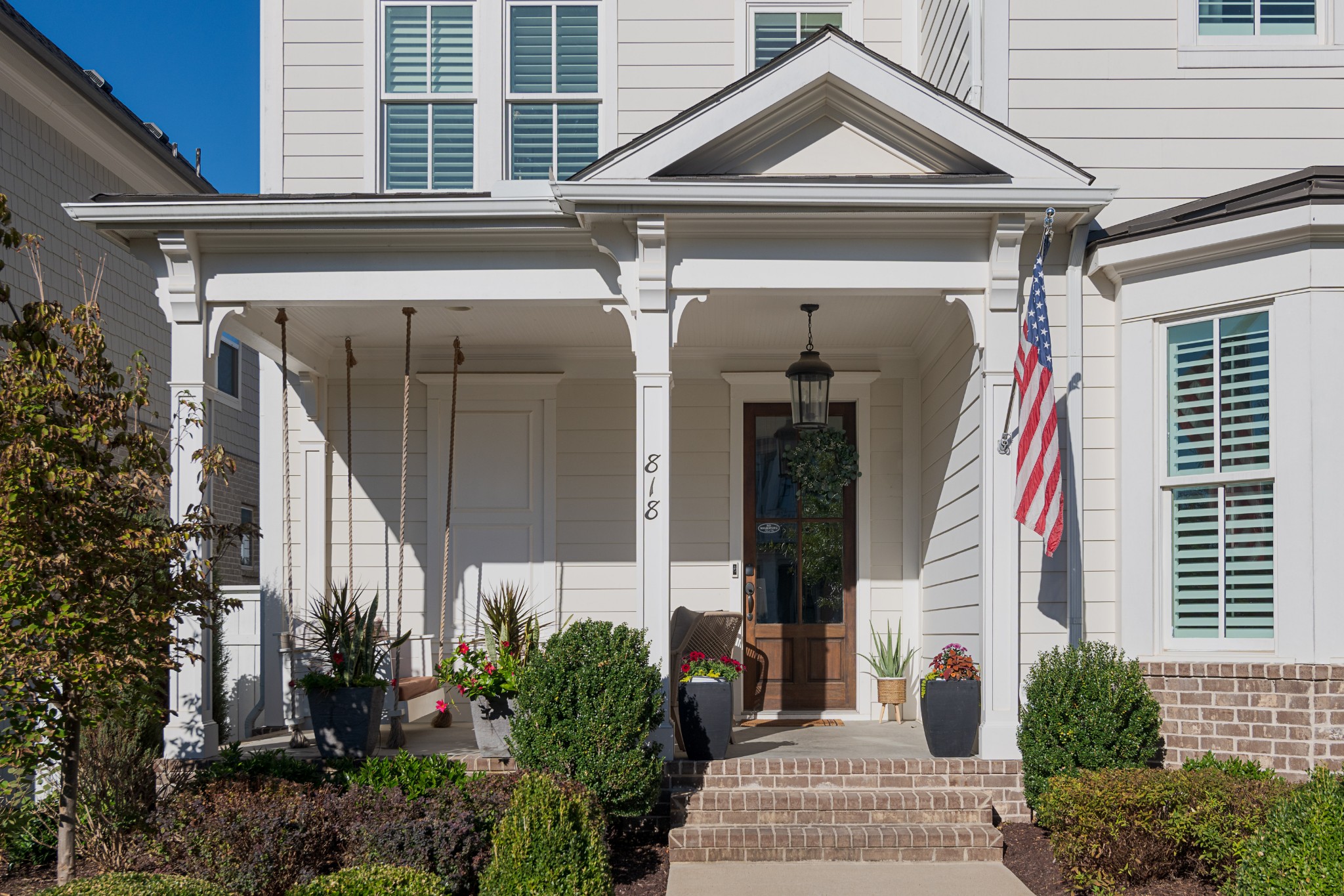 White home entrance with a covered porch, brick steps, hanging swing, and American flag.