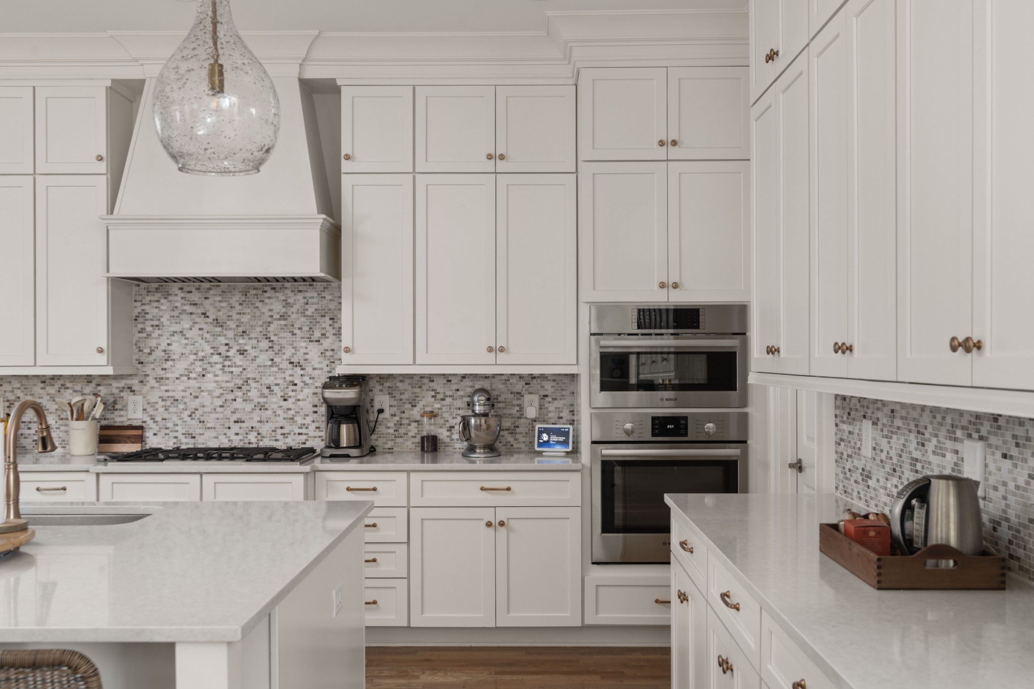 Bright kitchen with white cabinetry, mosaic tile backsplash, double ovens, and large quartz islands.