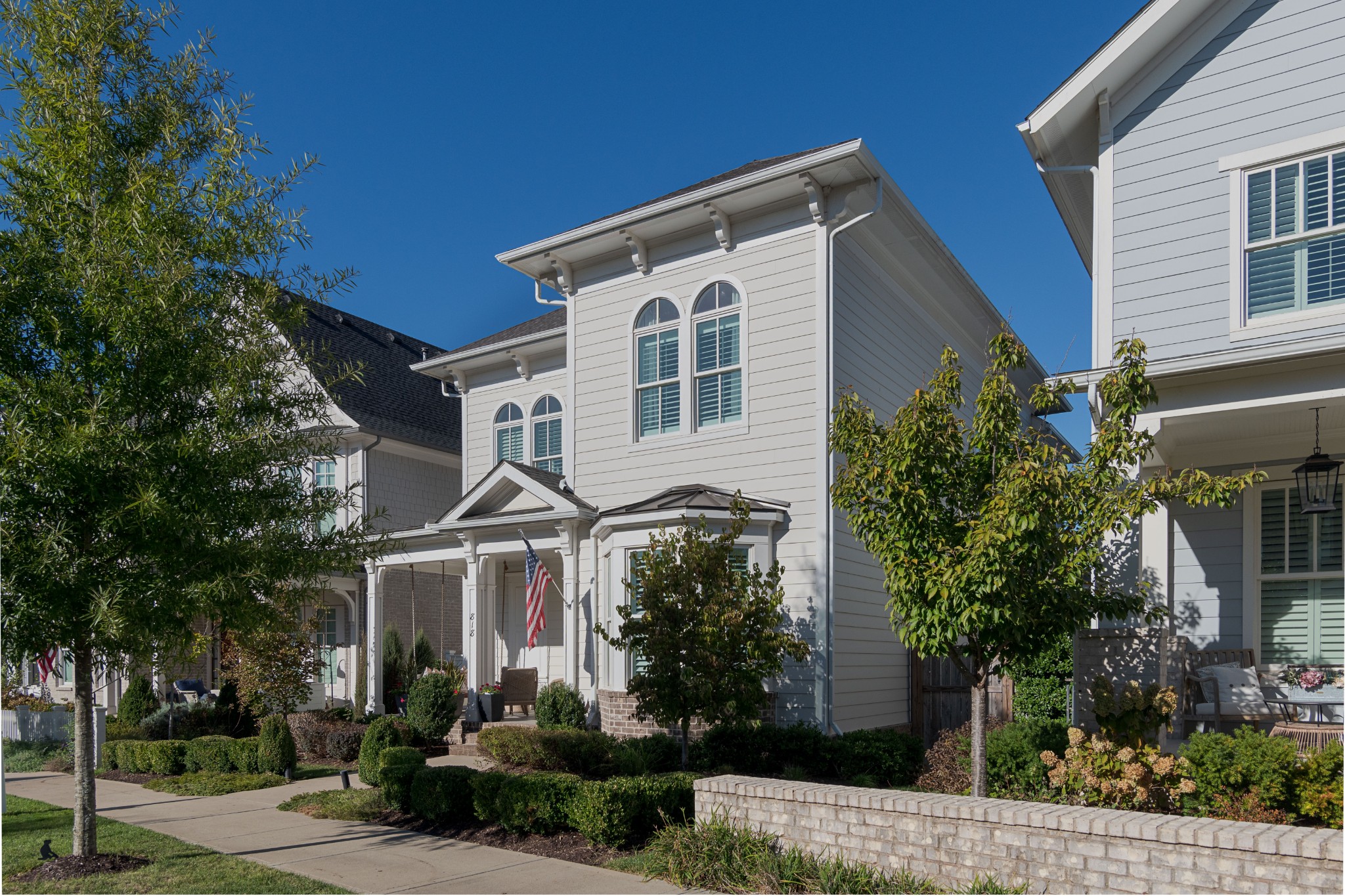 White two-story home with arched windows, a covered porch, and landscaped front yard.
