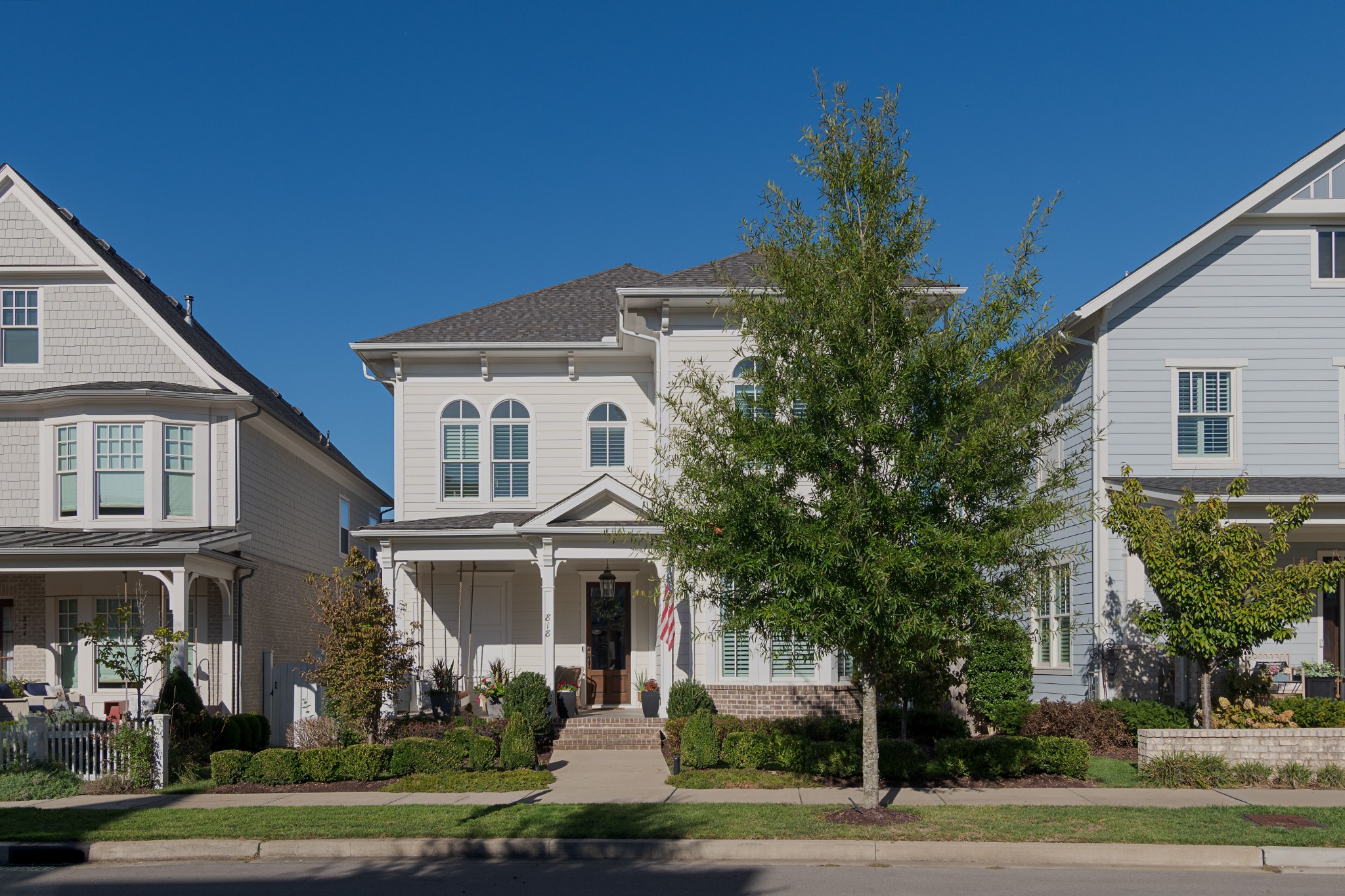 White two-story home with a covered front porch, arched windows, and a large tree in front.