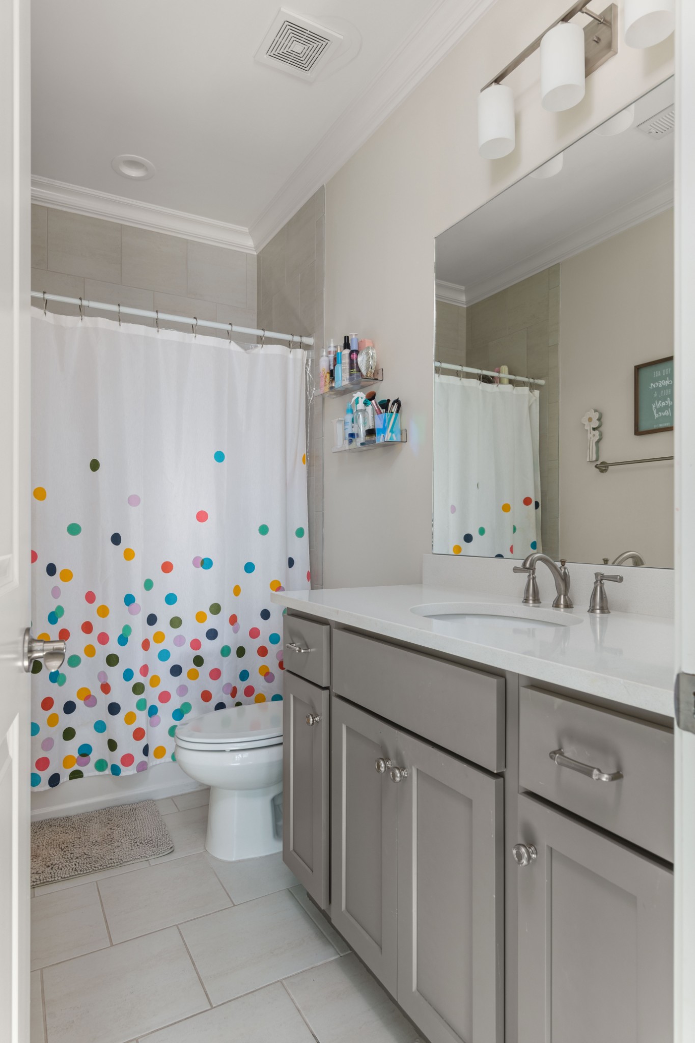 Bathroom with gray vanity, large mirror, and a colorful polka-dot shower curtain.