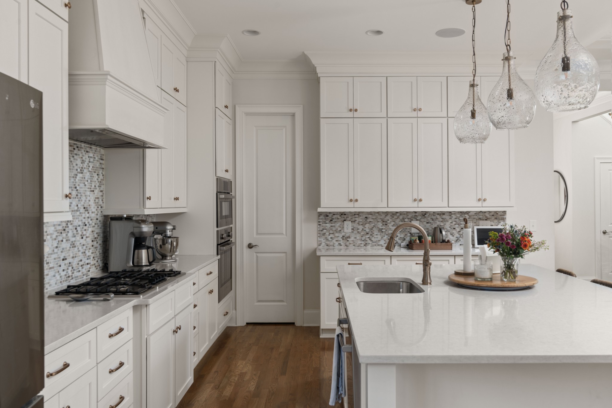 Bright white kitchen with a large quartz island, mosaic backsplash, and glass pendant lights.