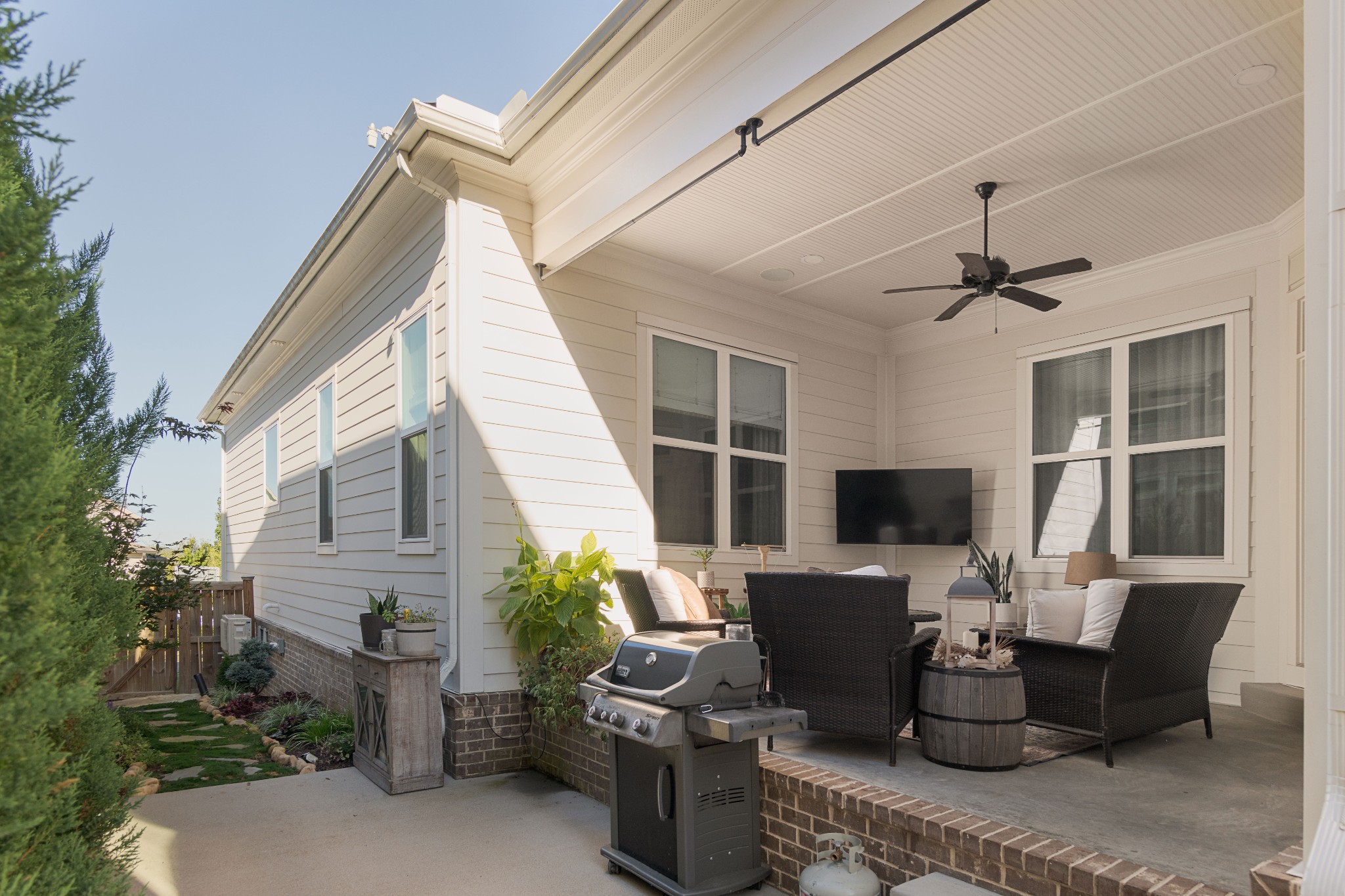 Covered patio with wicker seating, ceiling fan, and a gas grill beside the house.