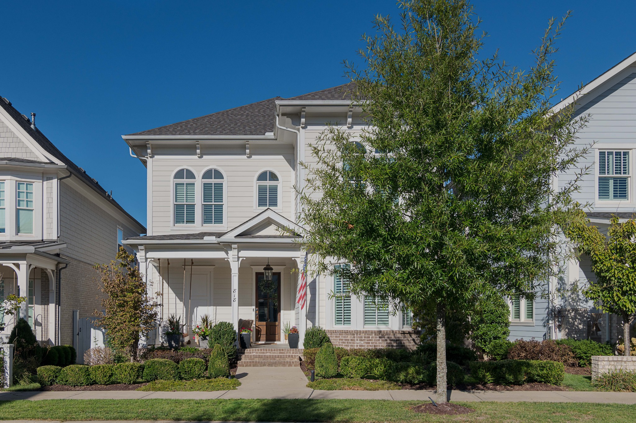 White two-story house with arched windows, a covered porch, and landscaped front yard.