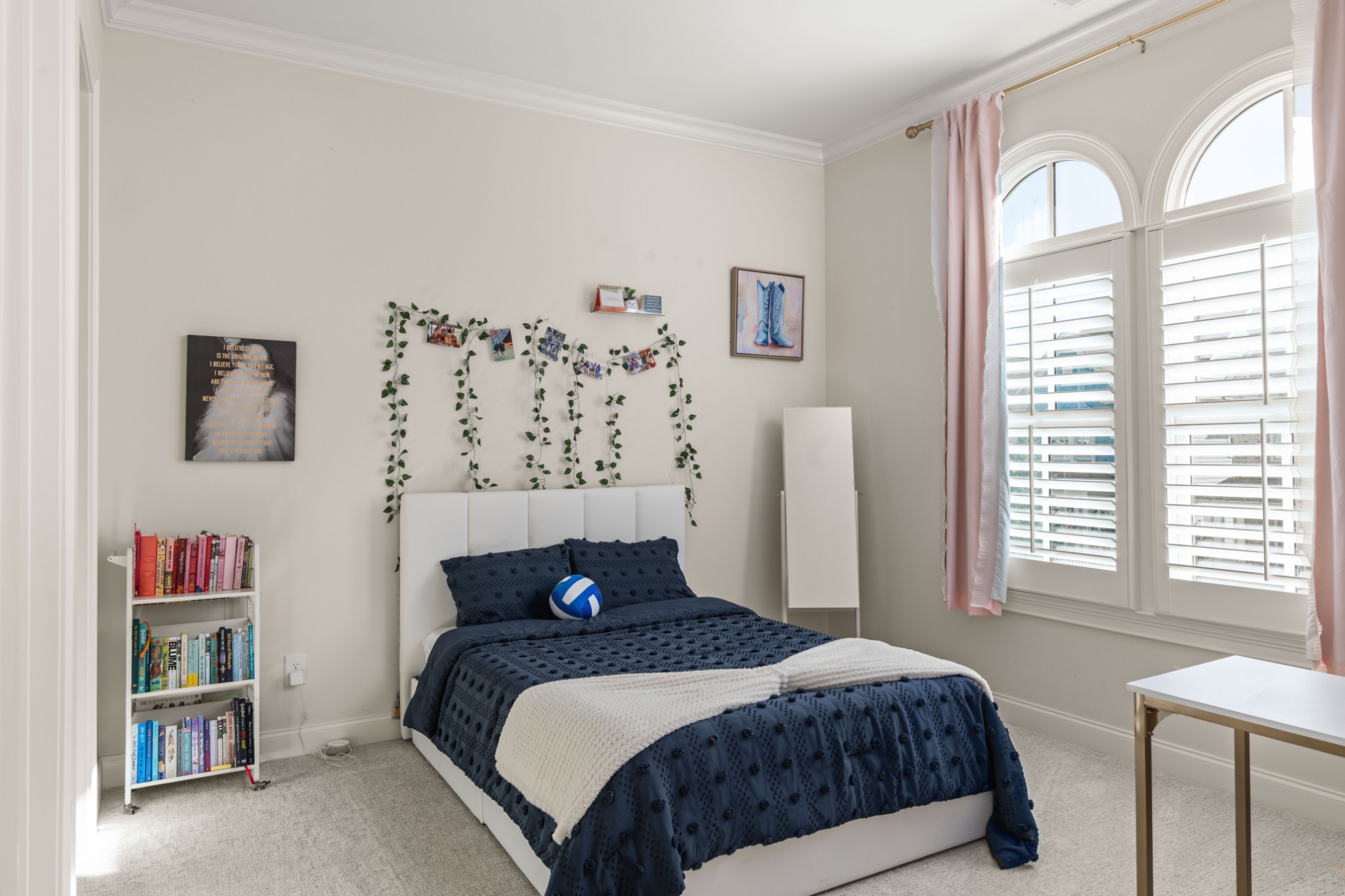 Bedroom with a navy bedspread, trailing wall greenery, and tall arched windows with shutters.