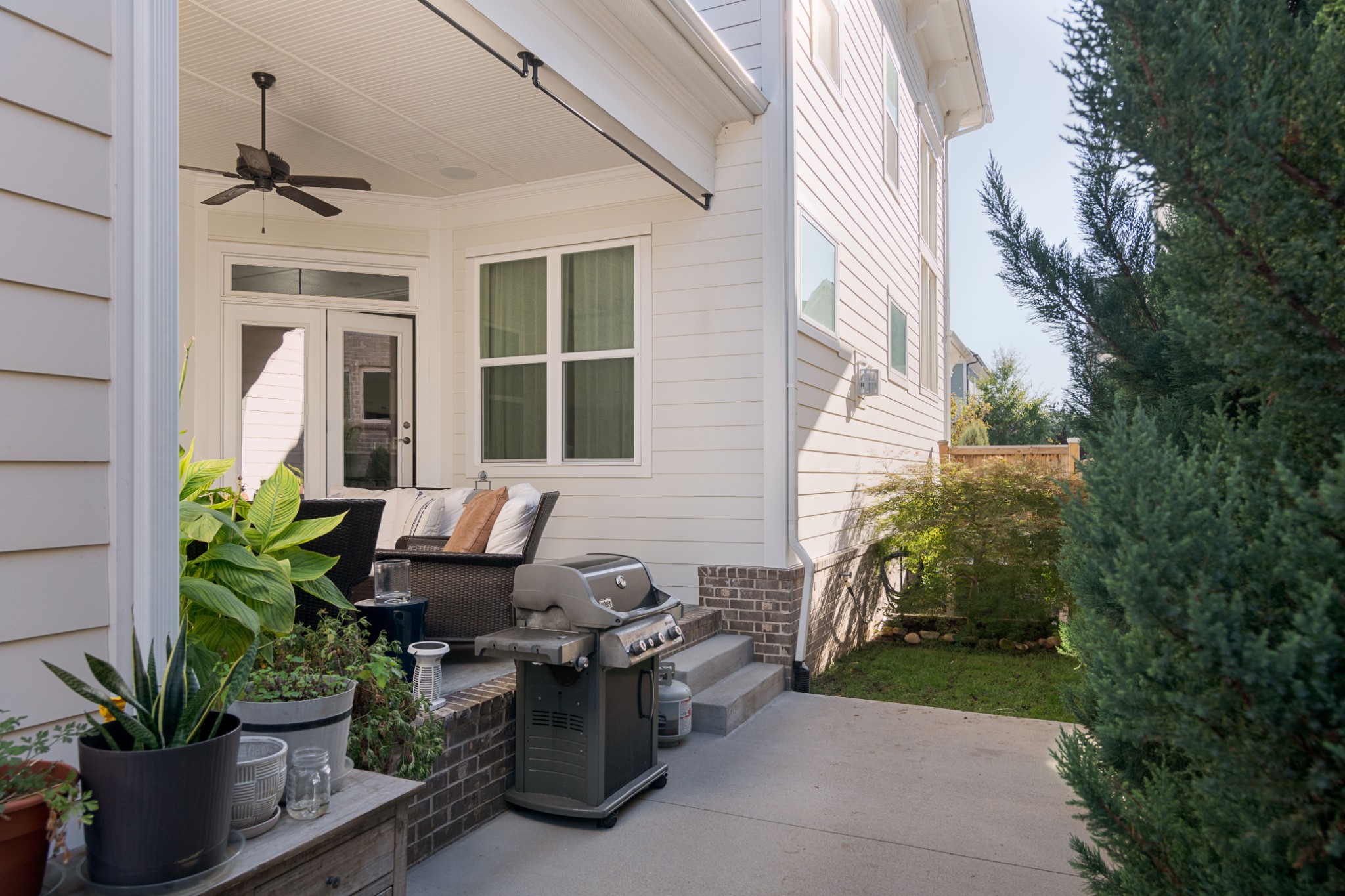 Covered backyard patio with outdoor seating, potted plants, and a barbecue grill.