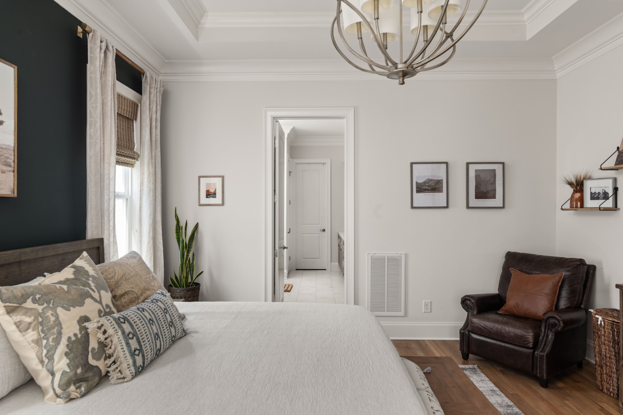 Staged bedroom with a dark accent wall, layered pillows, and a leather armchair.