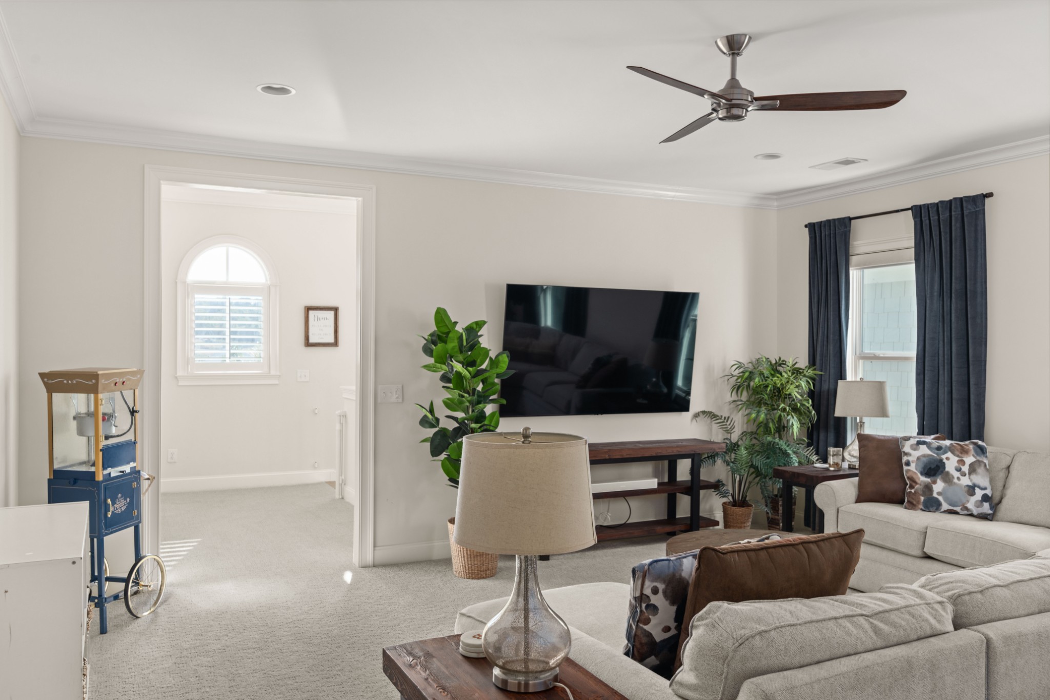 Furnished living room with a wall-mounted television, sectional sofa, ceiling fan, and popcorn machine.