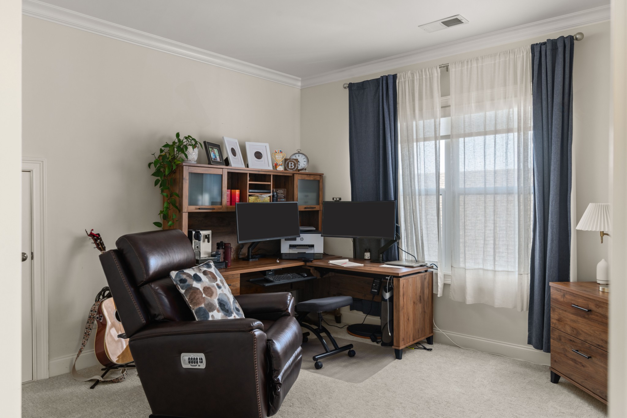Home office with a dual-monitor desk, dark leather recliner, and tall curtained window.