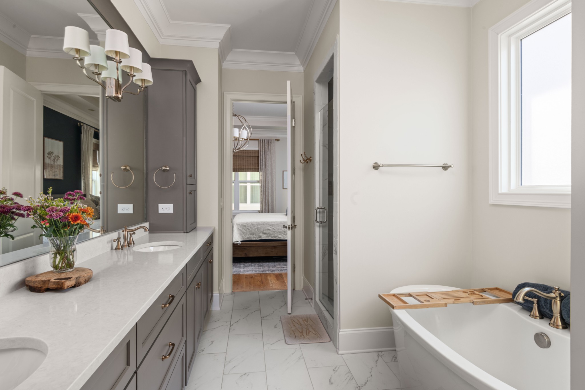Bathroom with a double vanity, marble-look tile, and a soaking tub beside a large window.