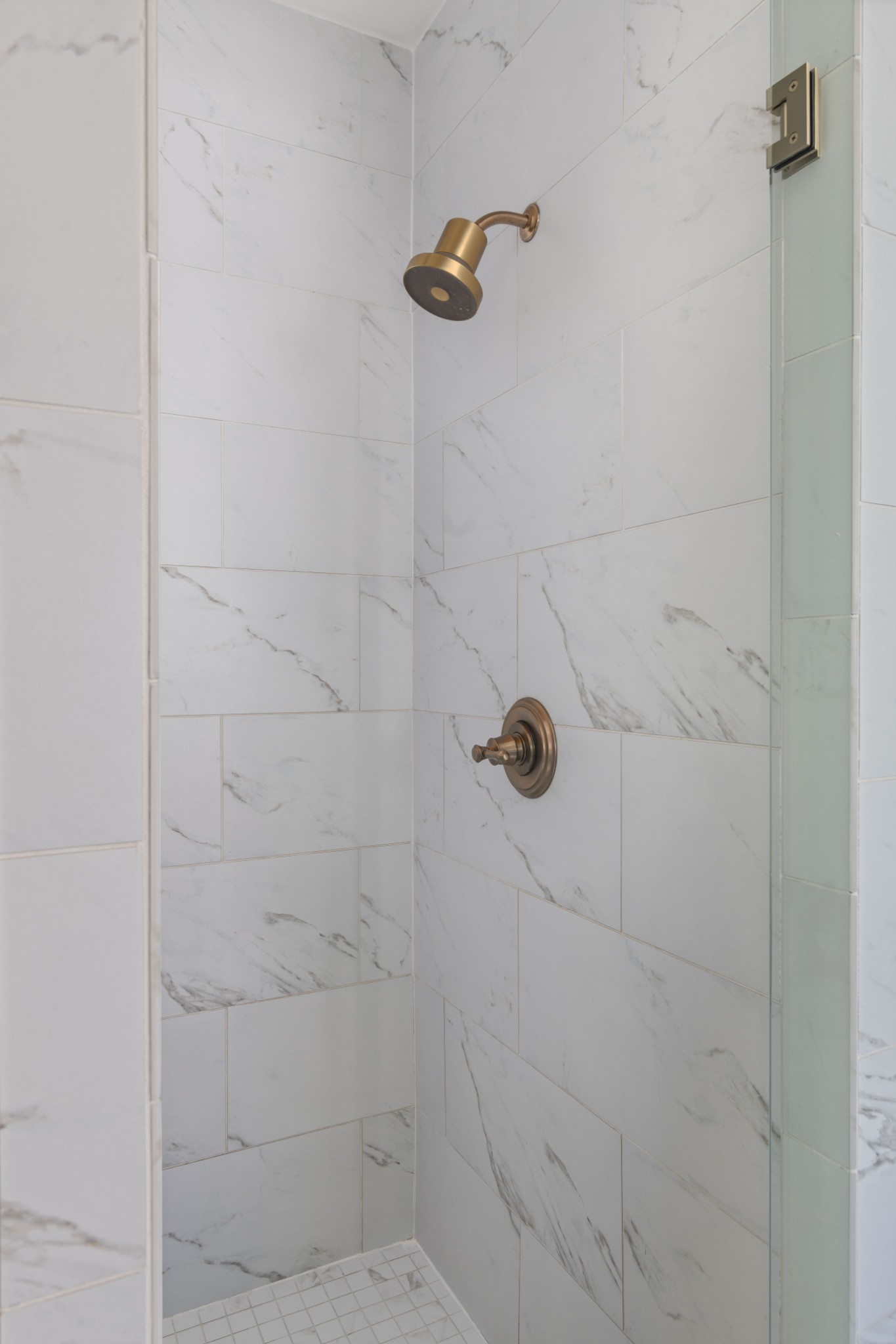 Walk-in shower with white veined tile, brass fixtures, and a glass panel.