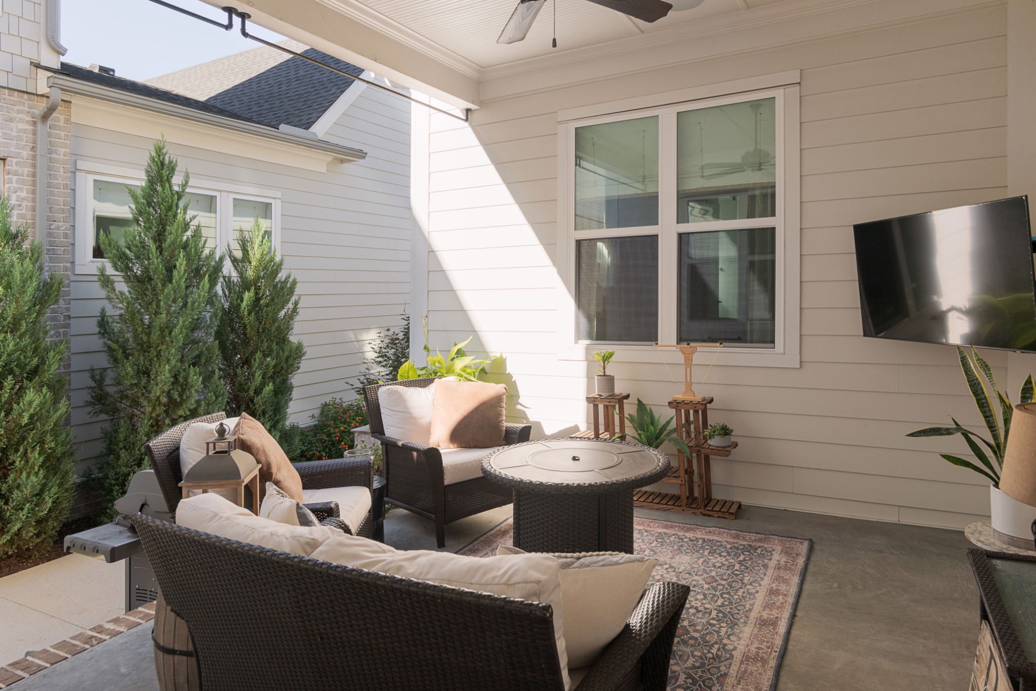 Covered patio with wicker seating, a round table, potted plants, and a wall-mounted television.