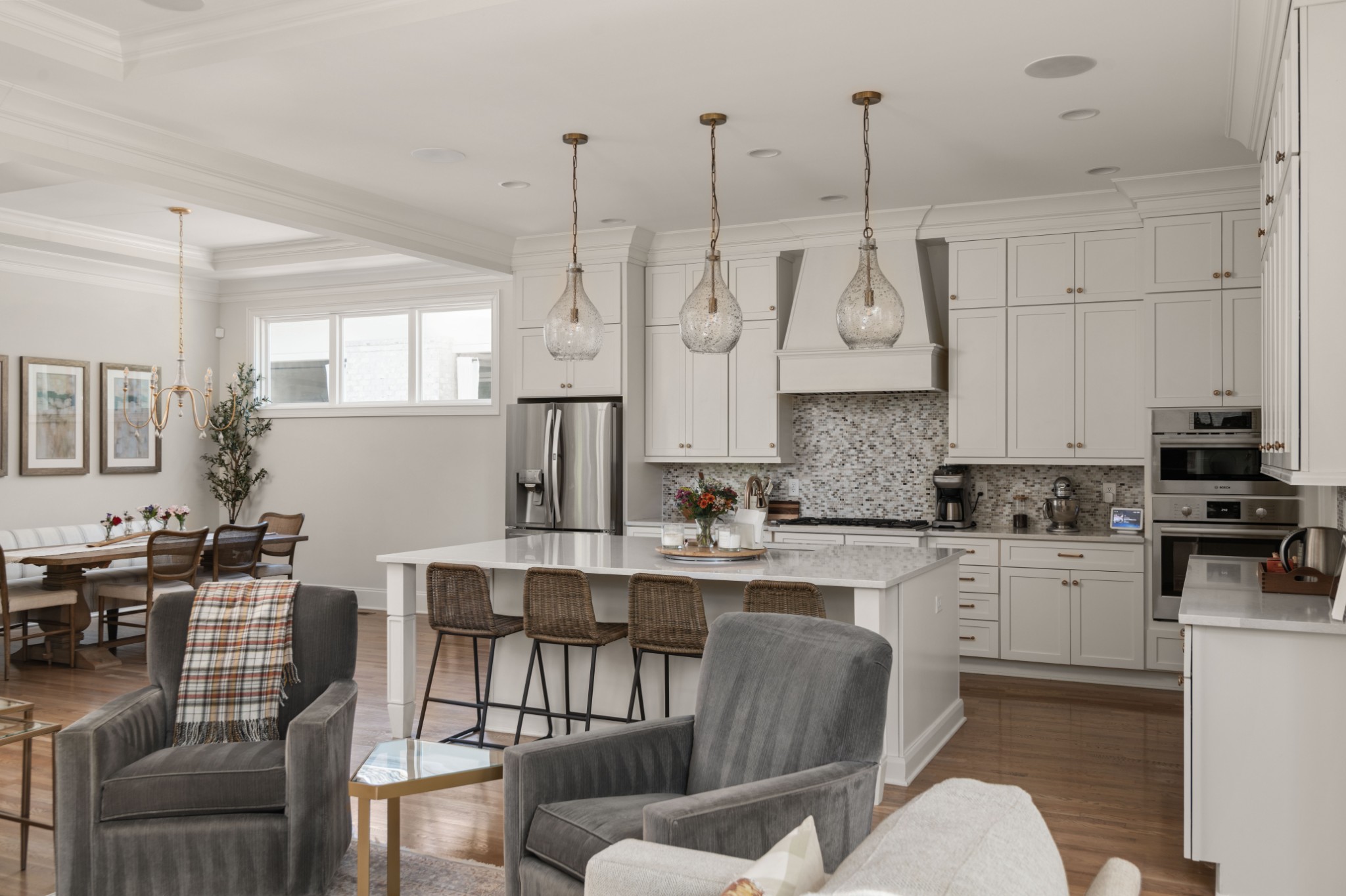Open kitchen with white cabinets, a large island, glass pendant lights, and an adjoining dining area.