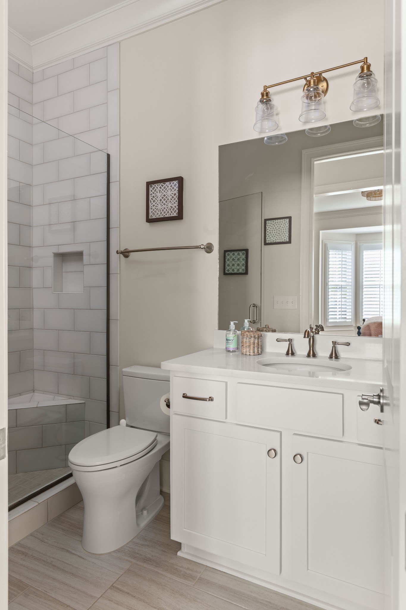 Bathroom with glass-enclosed tiled shower, white vanity, and brass three-light fixture.