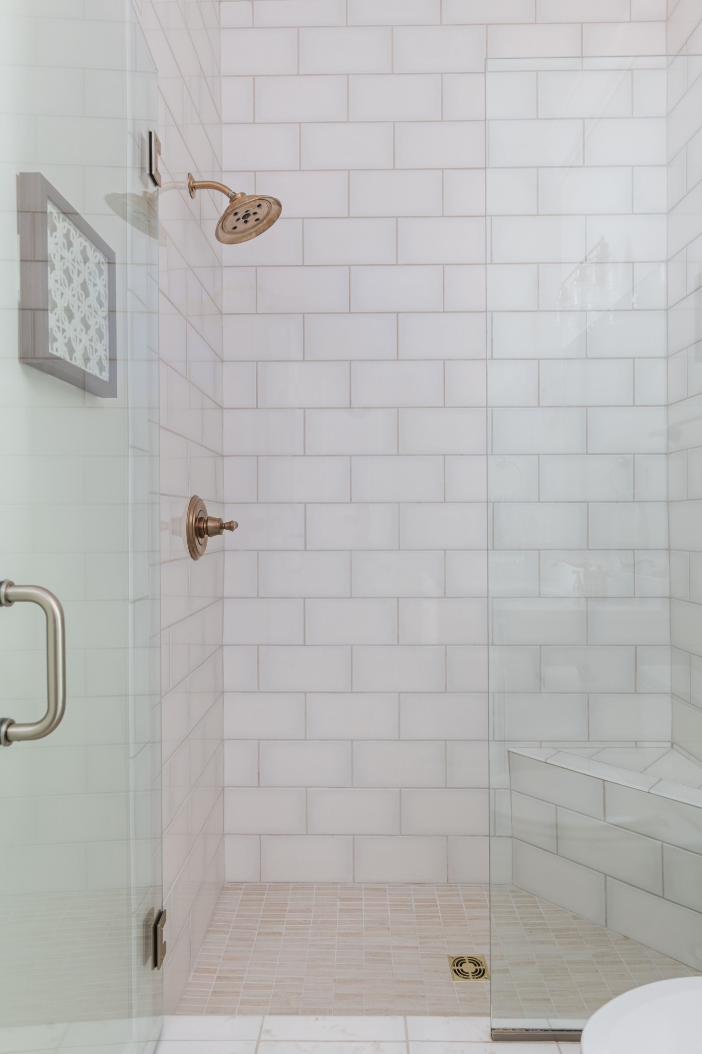 Walk-in shower with white subway tile, glass enclosure, bronze fixtures, and a built-in bench.