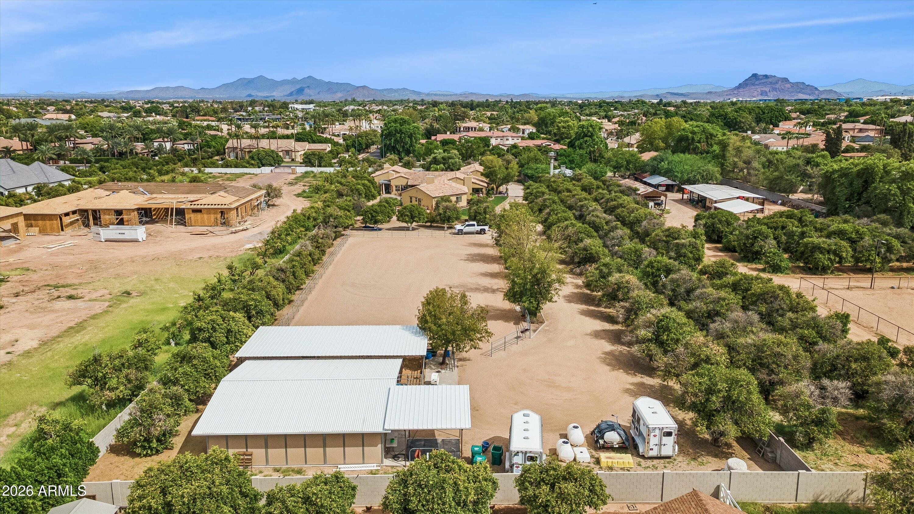 Aerial view of a Mesa equestrian property with a large dirt arena, covered structures, and distant mountains.