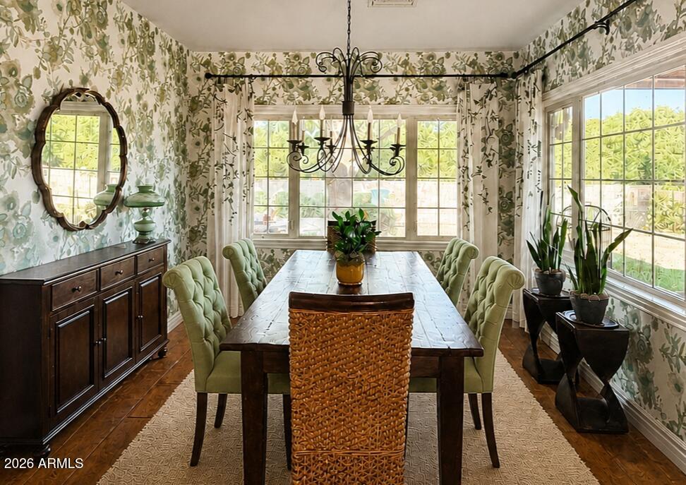 Dining room with a dark wood table, green tufted chairs, botanical wallpaper, and large sunny windows.