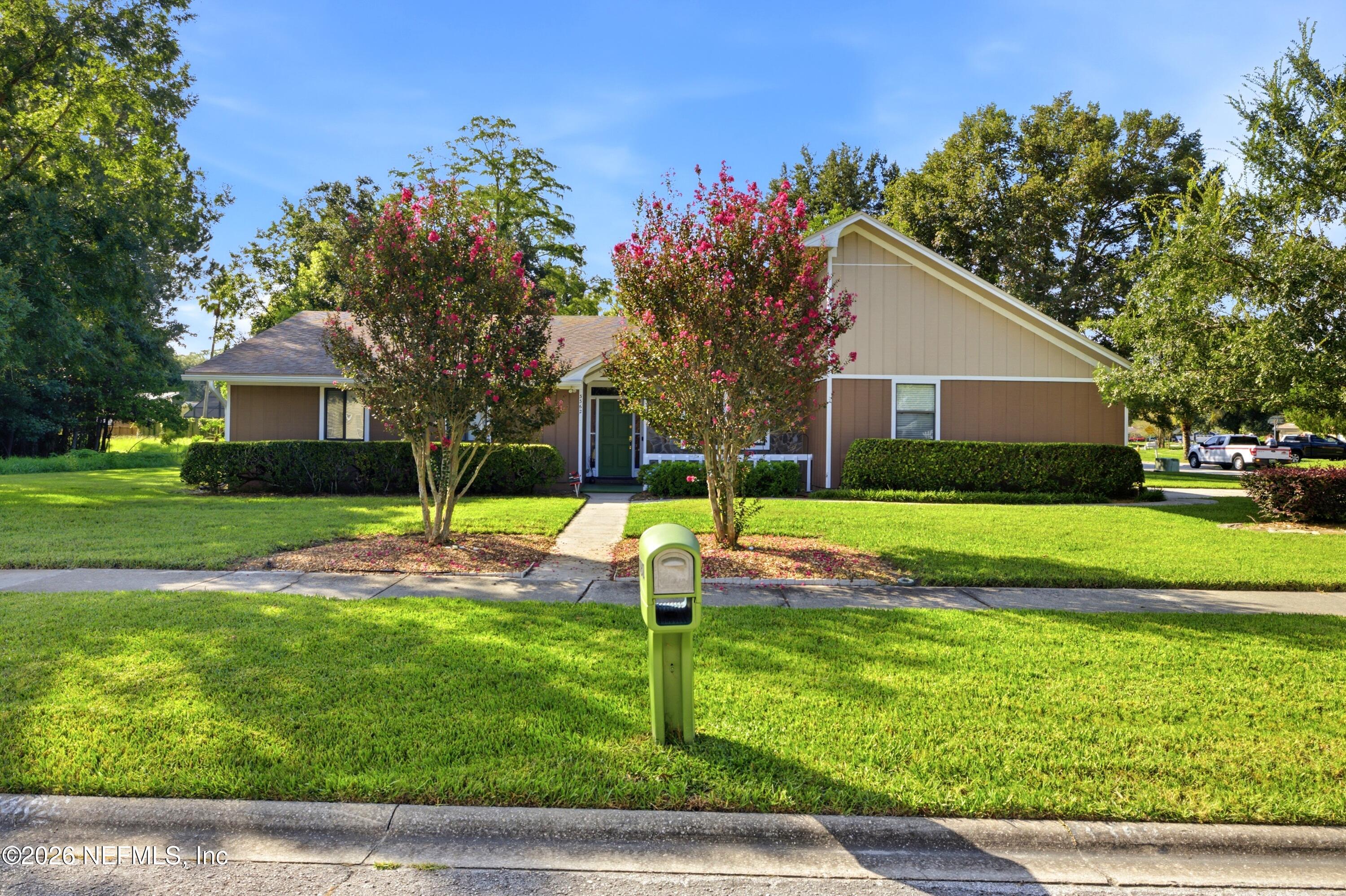 Single-story home with a gabled roof, pink flowering trees, and a mailbox beside the front walkway.