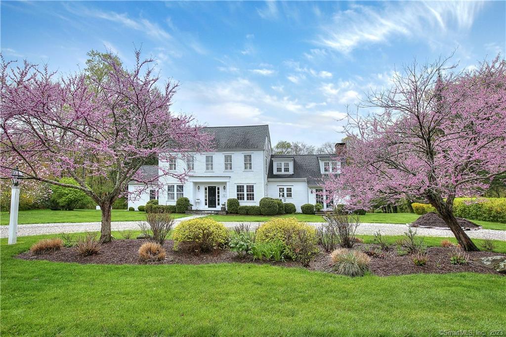 White two-story house framed by pink flowering trees and a landscaped lawn.