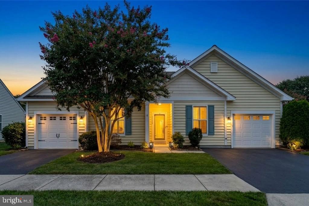 Single-story home at dusk with two garages, a glowing entry, and a flowering tree.