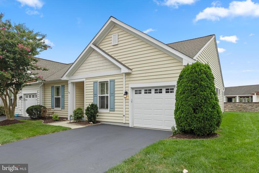 Beige home with blue shutters, attached garage, and landscaped driveway.