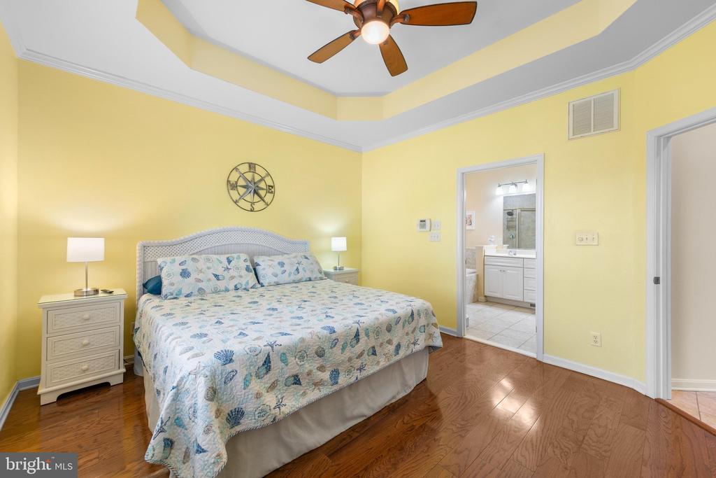 Bedroom with a shell-patterned bedspread, tray ceiling, and doorway to an ensuite bathroom.