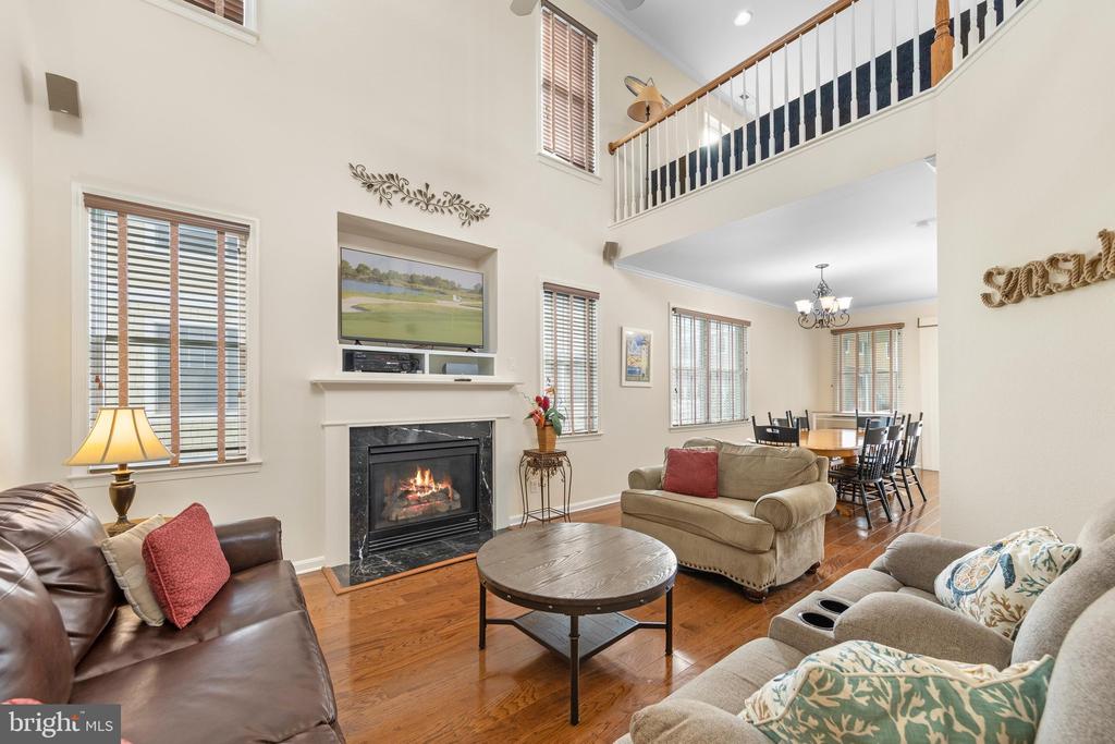 Living room with a fireplace, two-story windows, wood floors, and an open loft railing.