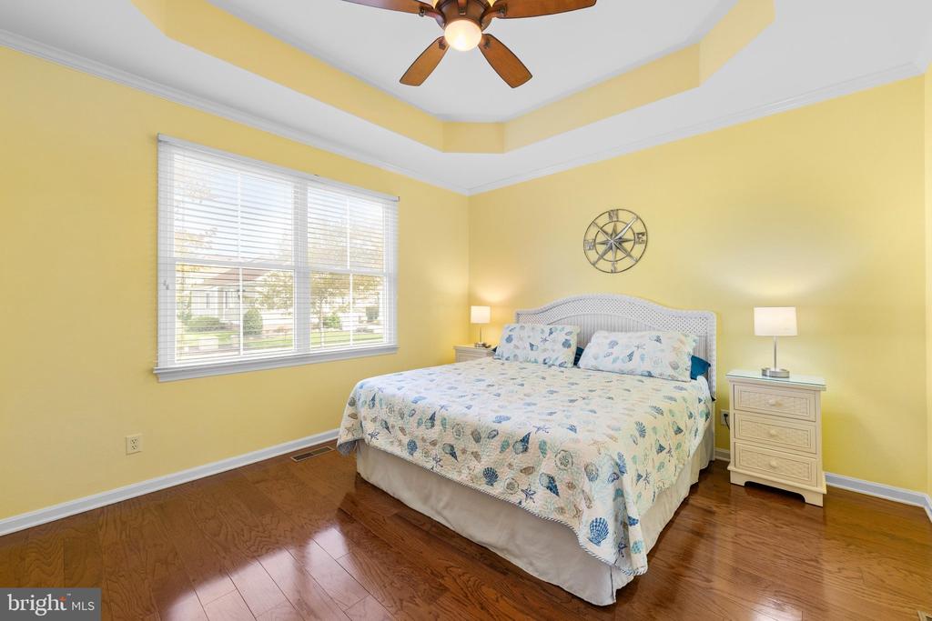 Bedroom with a floral-covered bed, yellow walls, hardwood floors, and a tray ceiling.
