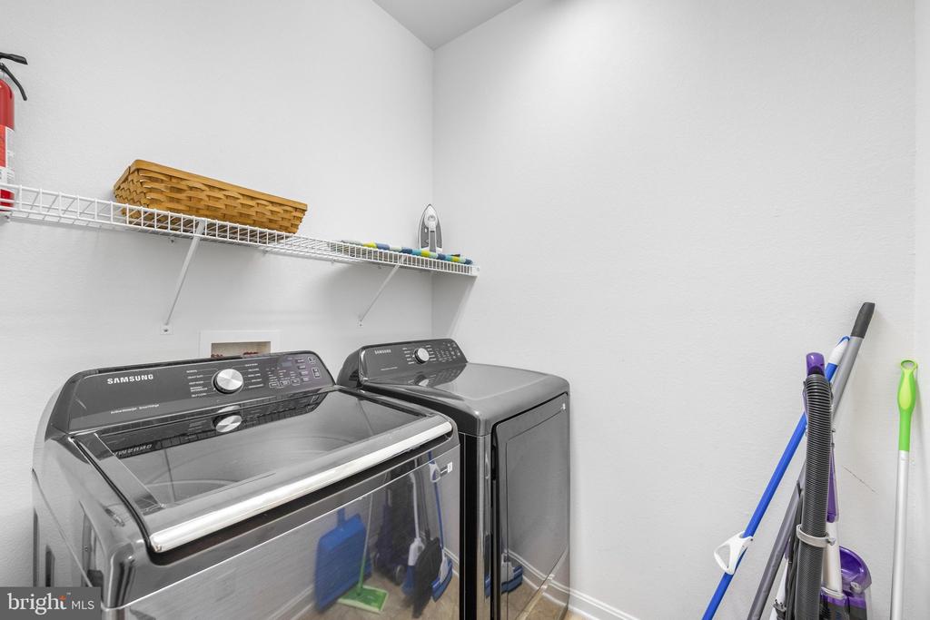 Laundry room with a front-loading washer and dryer beneath a storage shelf.