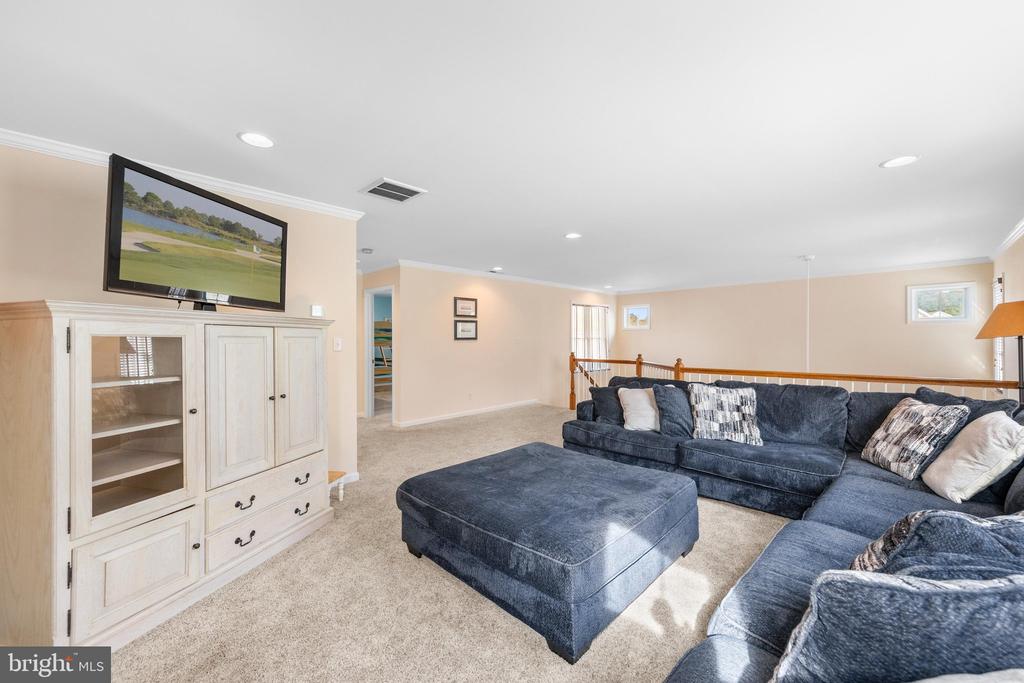 Carpeted upstairs lounge with a navy sectional, ottoman, and built-in media cabinet.
