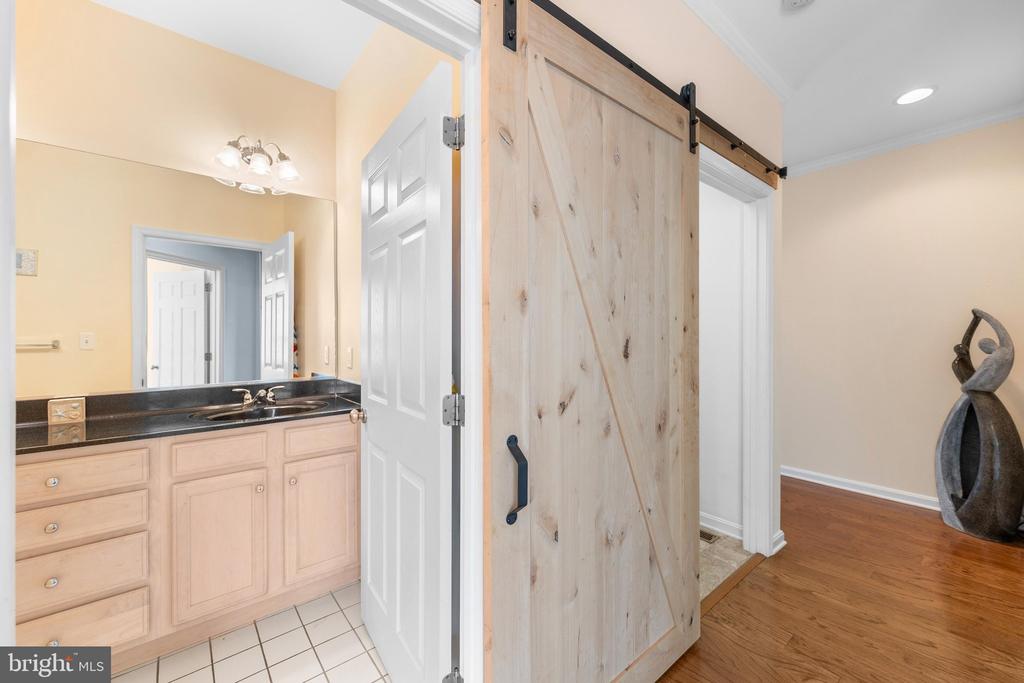 Bathroom vanity with dark countertop beside a natural wood sliding barn door.