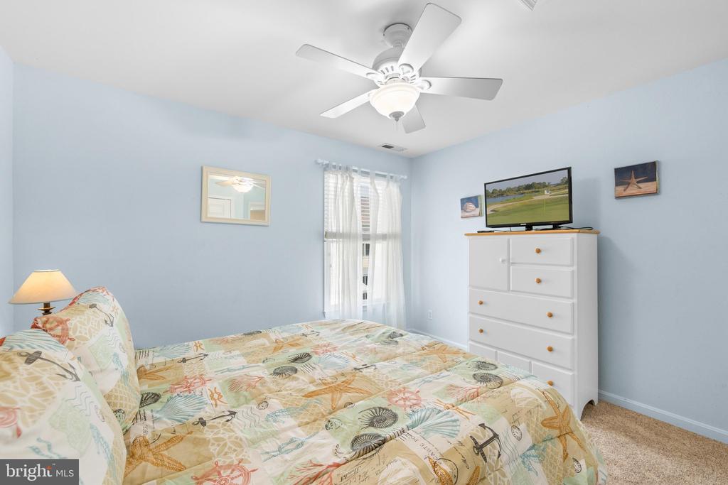 Bedroom with a patterned bedspread, white dresser, and television beneath a ceiling fan.
