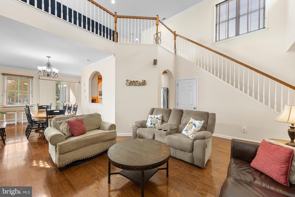 Furnished living room with a staircase, vaulted ceiling, and adjoining dining area.