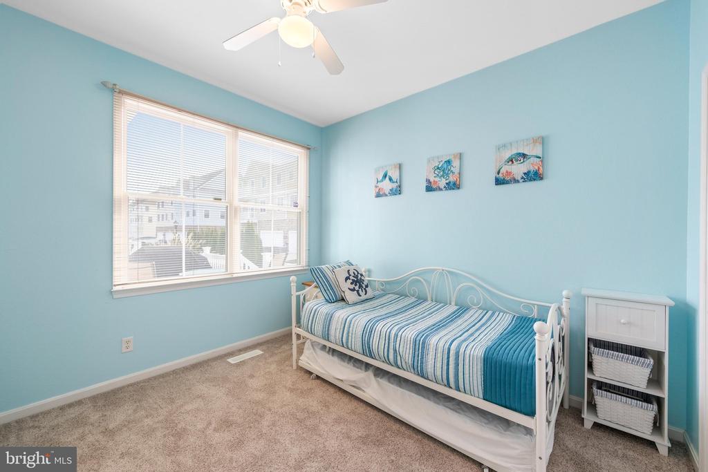 Blue bedroom with a white daybed, striped bedding, large window, and ceiling fan.