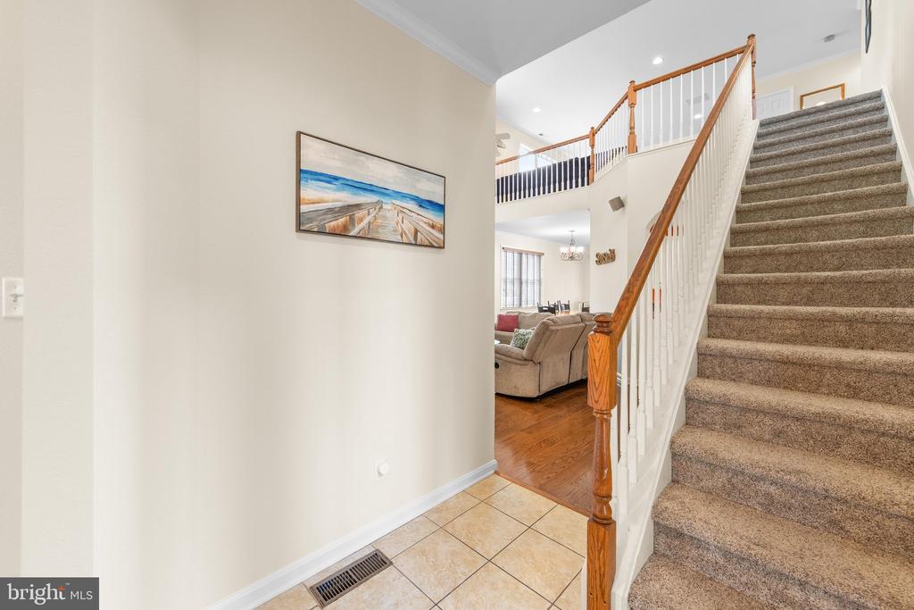 Entry foyer with tiled floor, carpeted staircase, and view into a furnished living room.