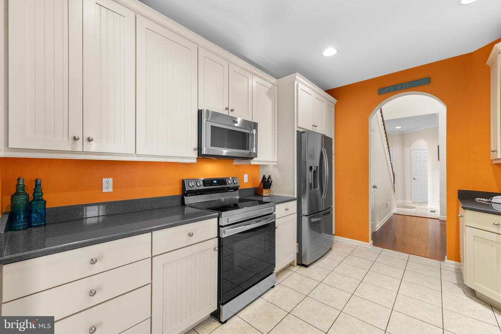 Kitchen with white cabinets, stainless steel appliances, dark counters, and a bright orange accent wall.
