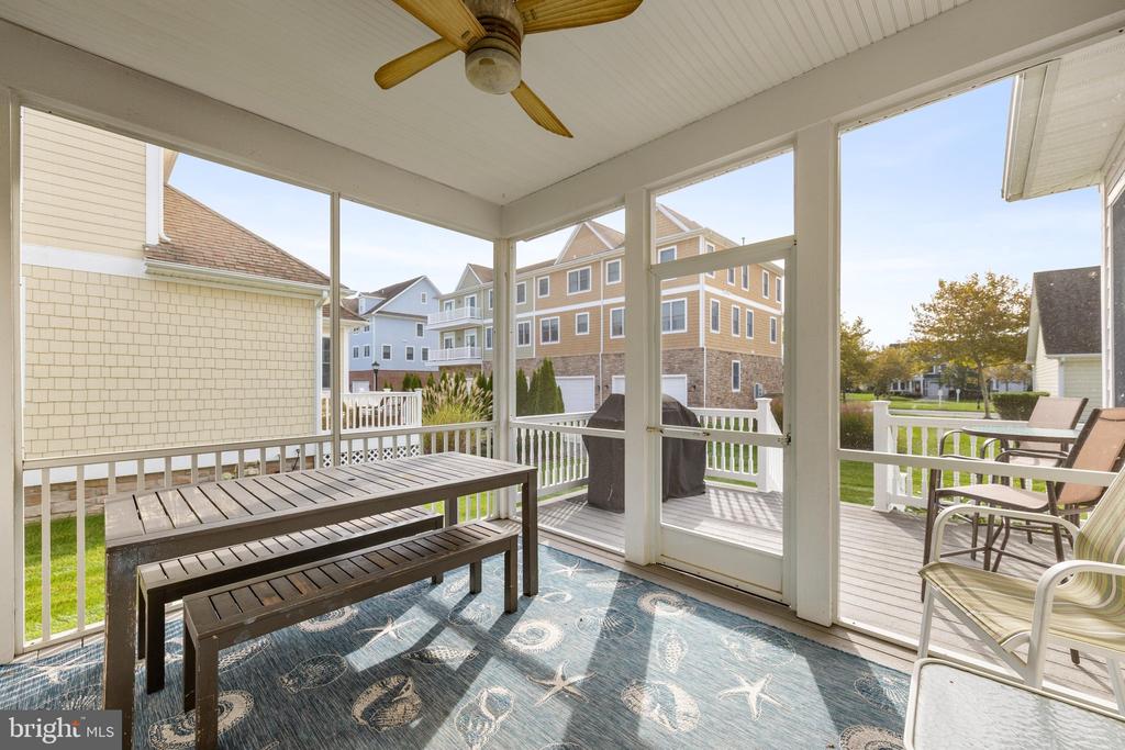 Screened porch with a ceiling fan, picnic-style table, and views of neighboring homes.