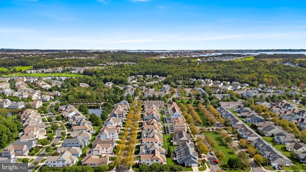 Aerial view of a residential neighborhood with wooded areas and distant water.
